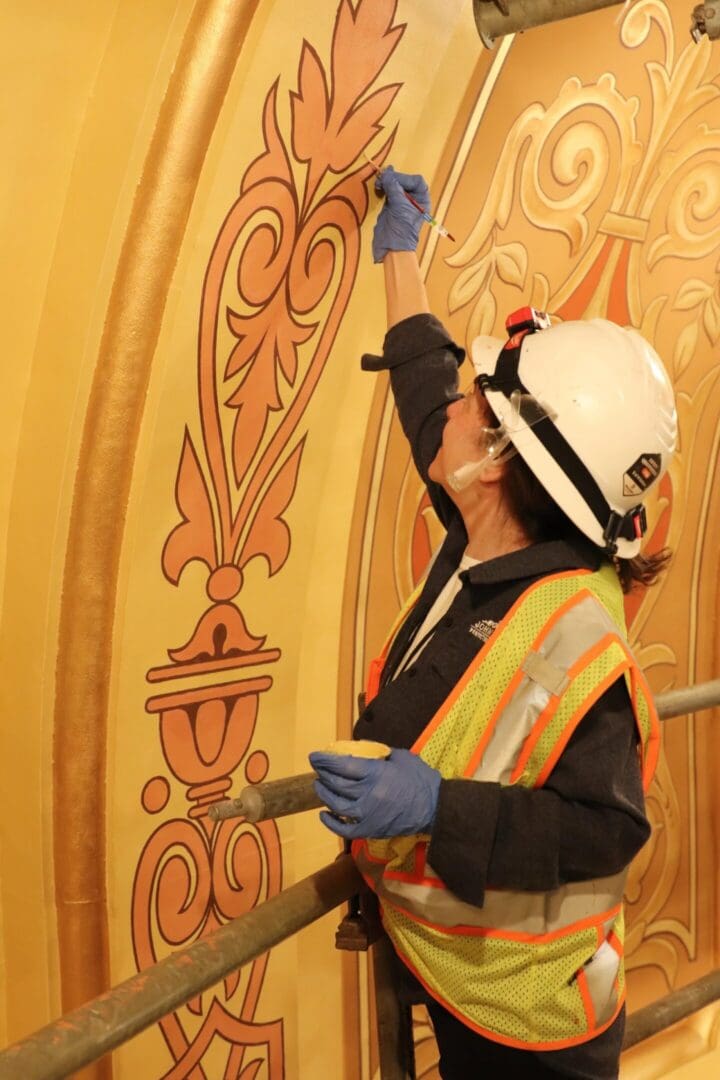 Worker painting ornate gold wall mural